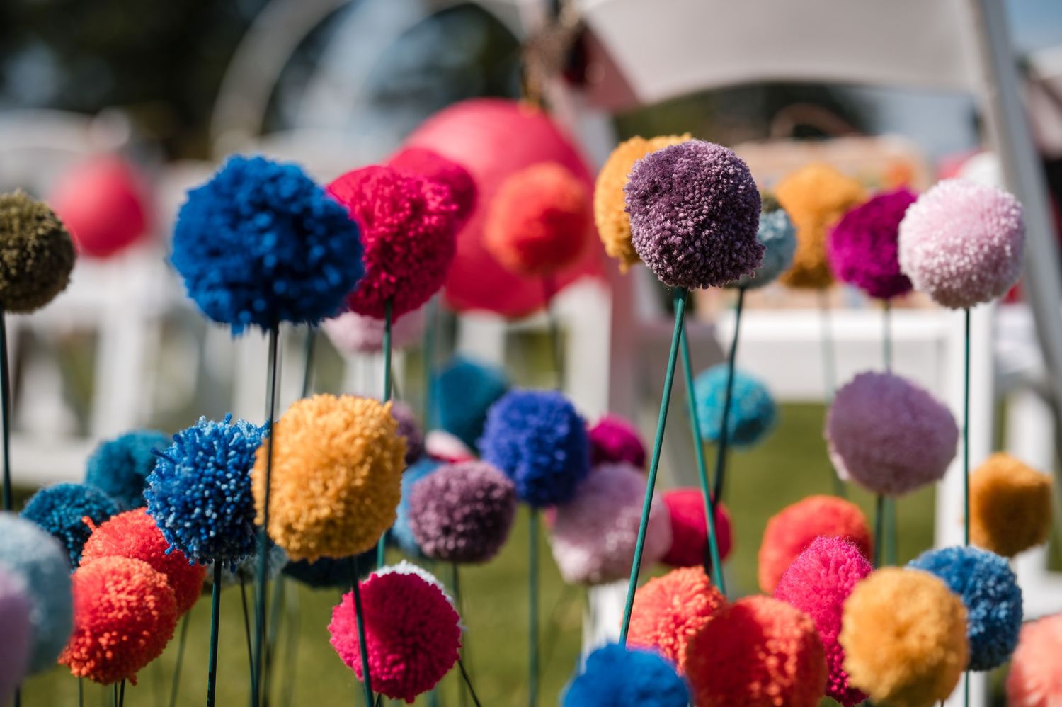Colorful pom pom decorations in bright pink, blue, and orange colors displayed outdoors against a blue sky.