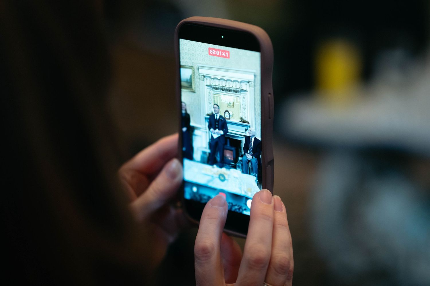 Someone holds a smartphone displaying a video or photo in a dimly lit environment.
