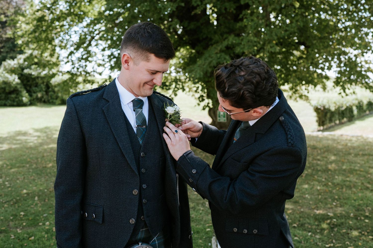 Wedding party in traditional Scottish formal wear laughing together outdoors.