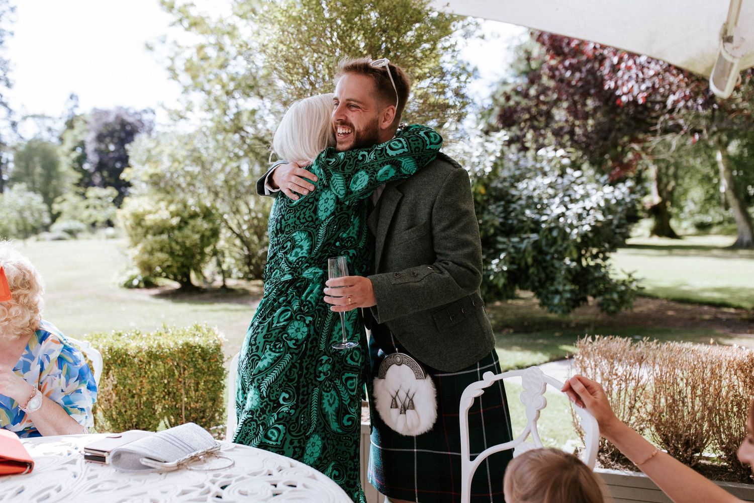 Wedding guests sharing an emotional embrace at an outdoor garden reception.