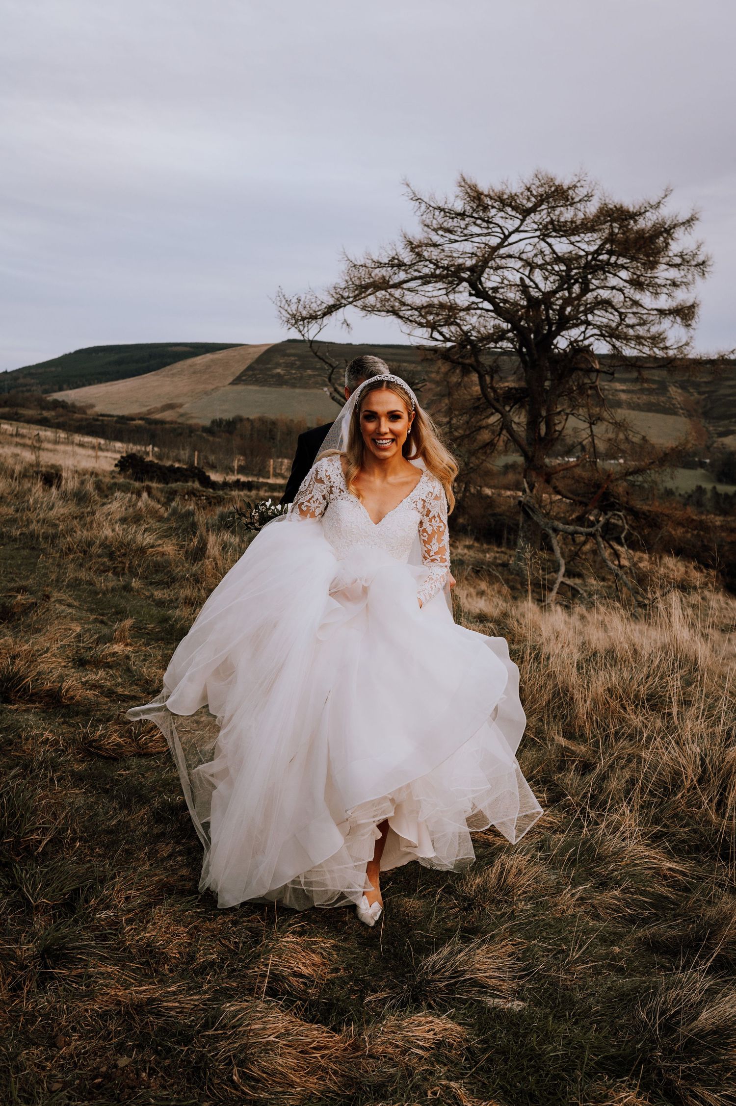 Aberdeen Wedding Photography. An elegant white wedding dress flowing in the wind against a backdrop of rustic countryside hills.