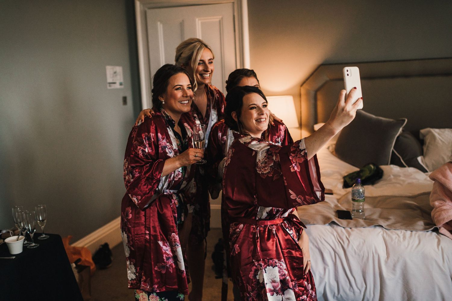 Wedding party members in burgundy floral robes taking a selfie during preparation.