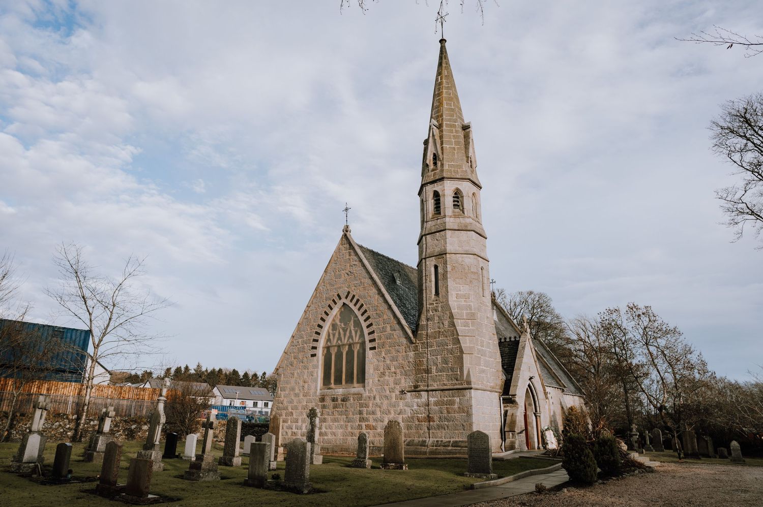 Stone church with tall spire and Gothic architecture photographed against a cloudy sky.