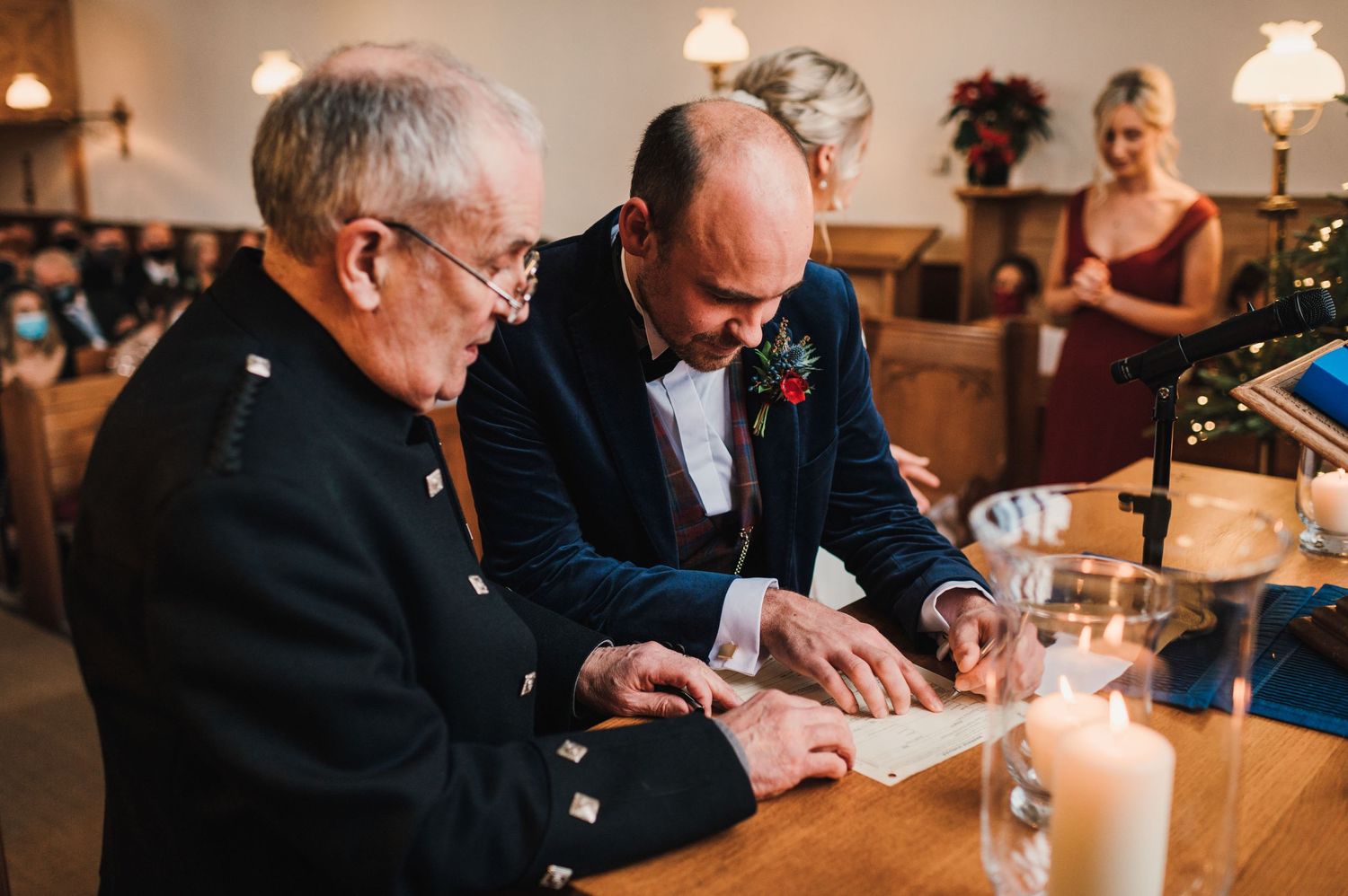 Attendees signing documents at church altar with glowing candle and vintage lamp.