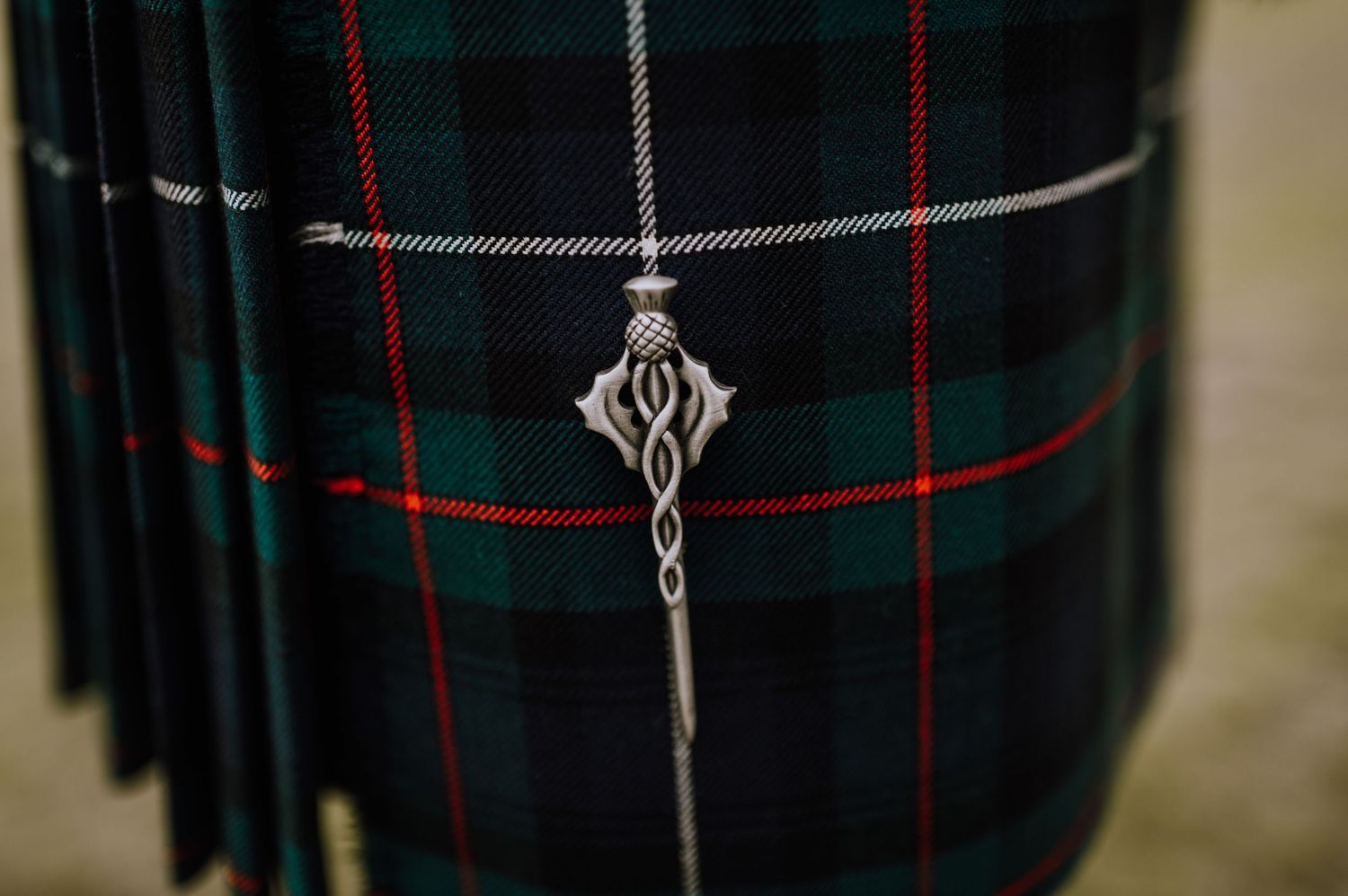 Close-up of an ornate silver kilt pin on traditional tartan plaid fabric.