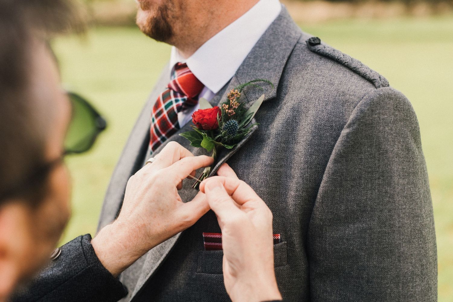 Hands pinning red and green boutonniere onto grey suit lapel.