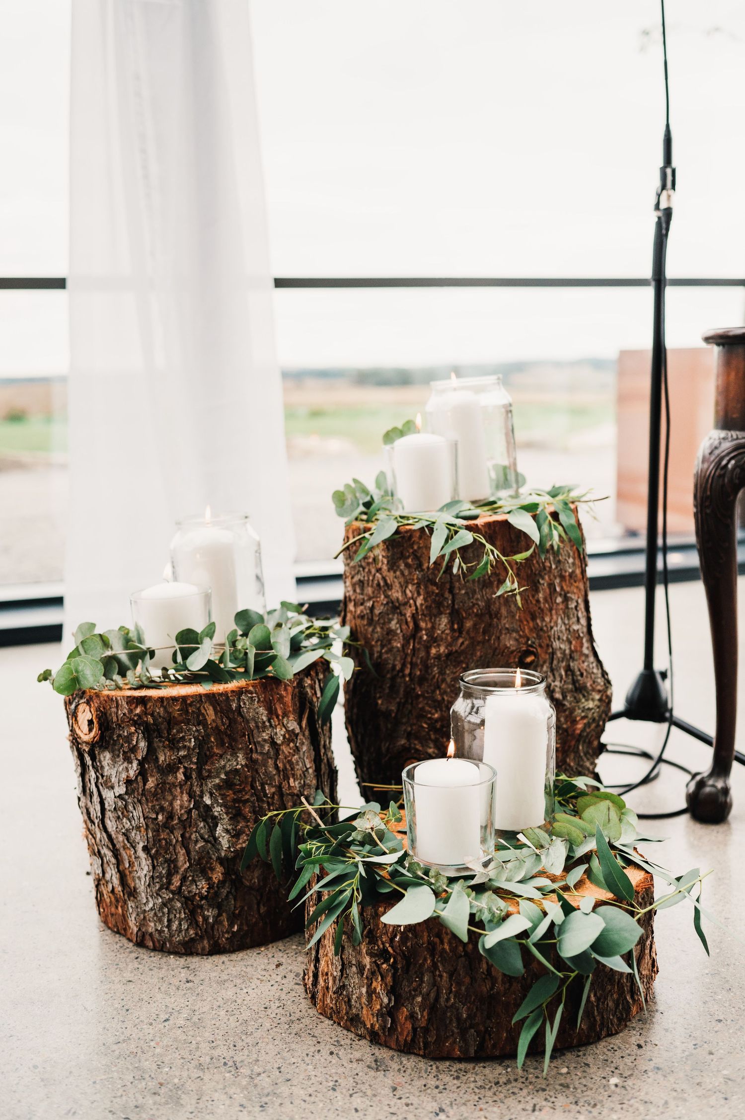Rustic wood log centerpieces decorated with white candles and greenery on a windowsill.