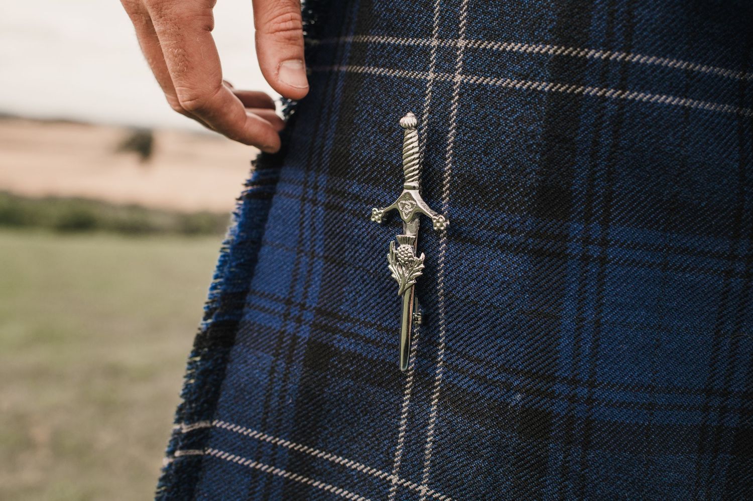 Close-up detail of a traditional Scottish kilt pin attached to blue and black tartan plaid fabric.