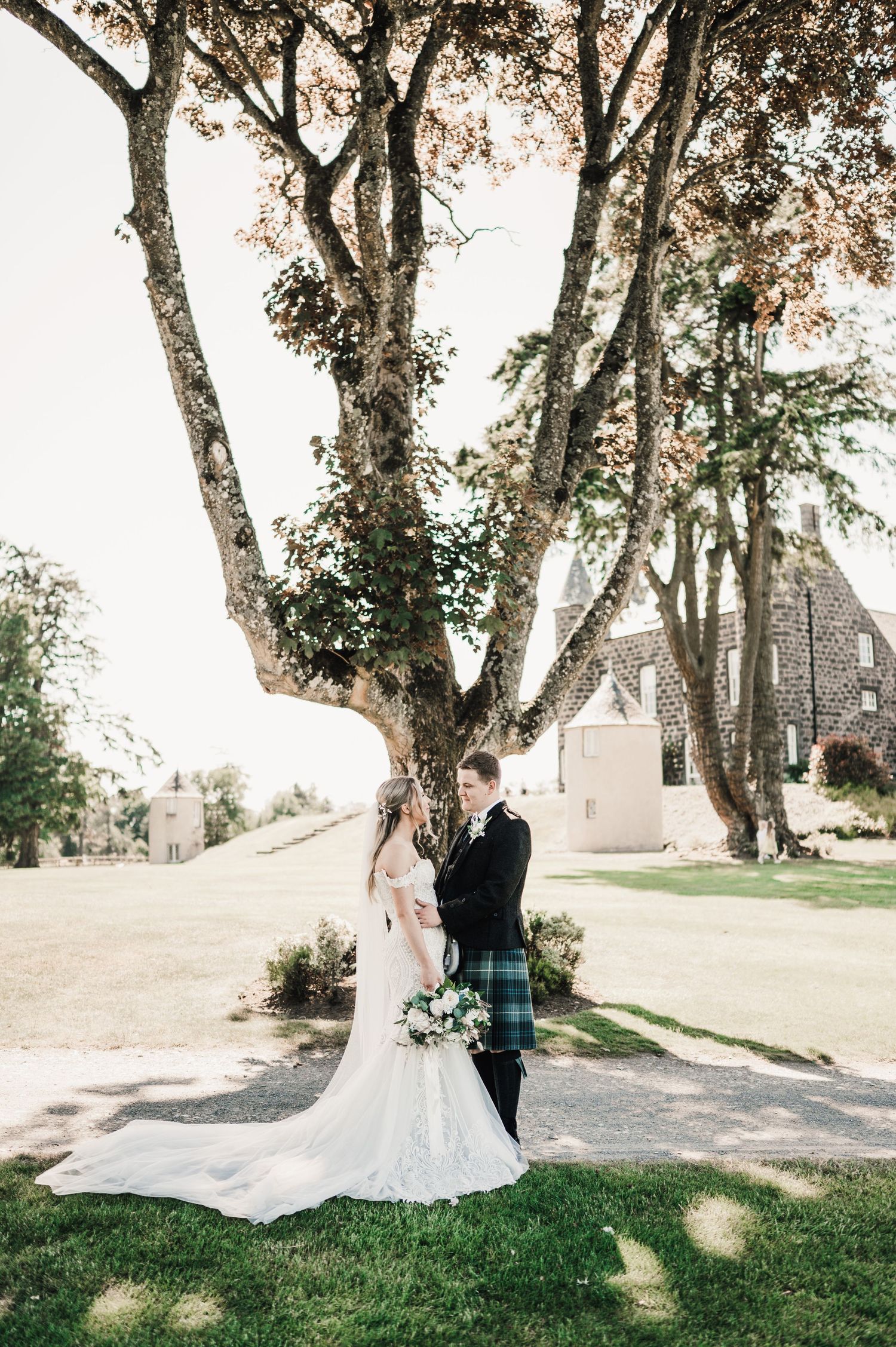Elegant wedding portrait beneath towering trees with castle in background.