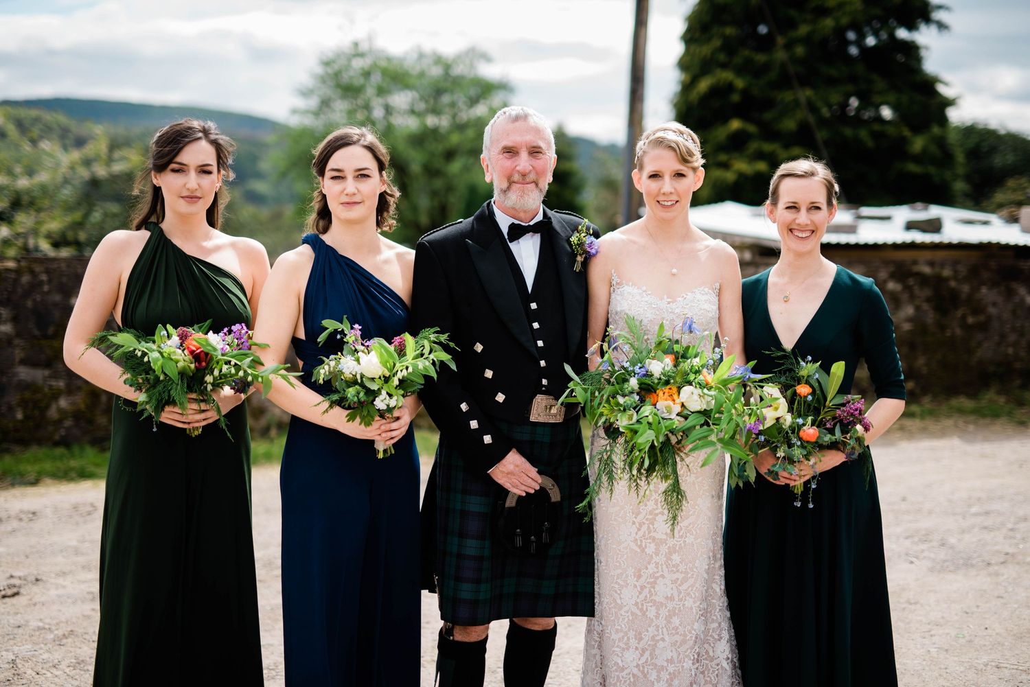 Wedding party with bridesmaids in elegant dark dresses and Scottish formal attire.