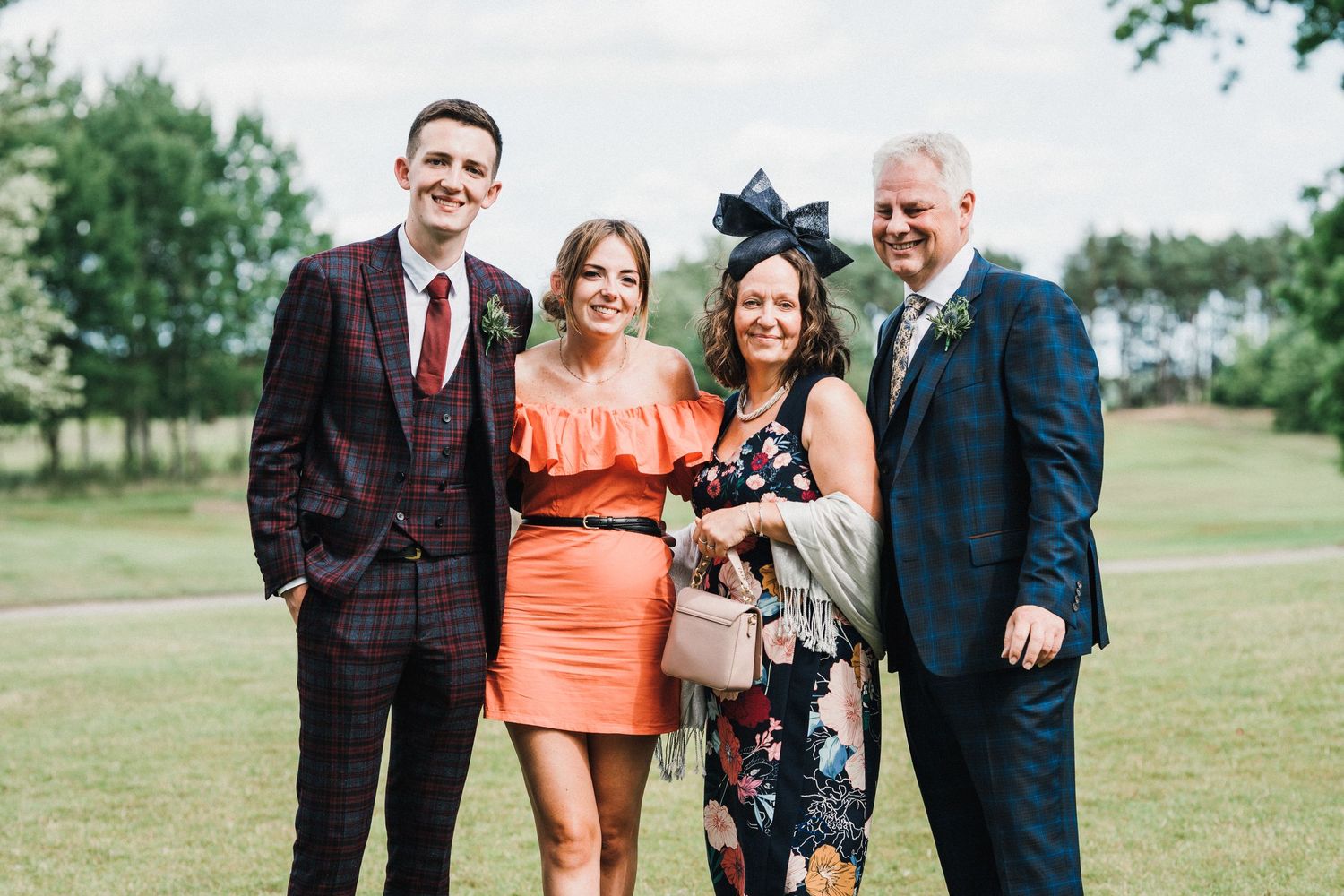 Group of wedding guests in formal attire posing together on a grassy lawn.