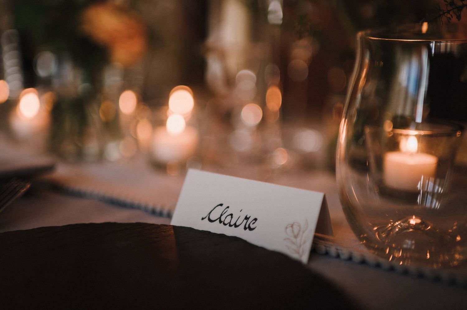An elegant place card setting at a wedding reception with candlelight and wine glass.