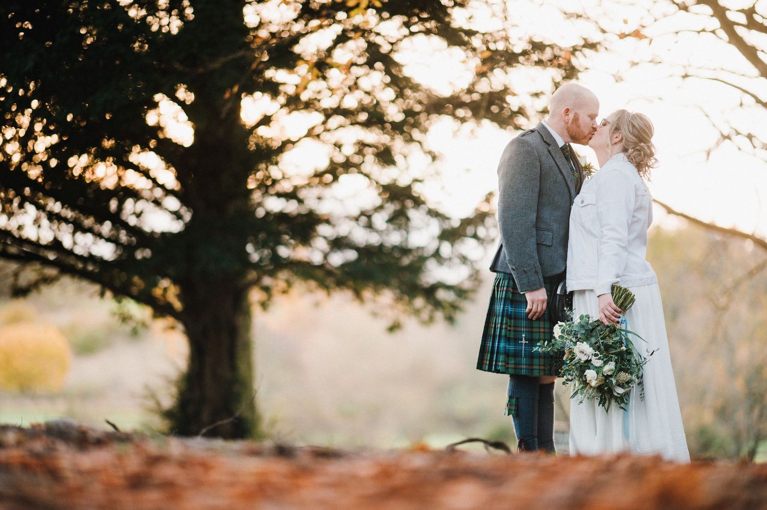 A Scottish wedding couple shares an intimate moment against an autumn sunset backdrop.
