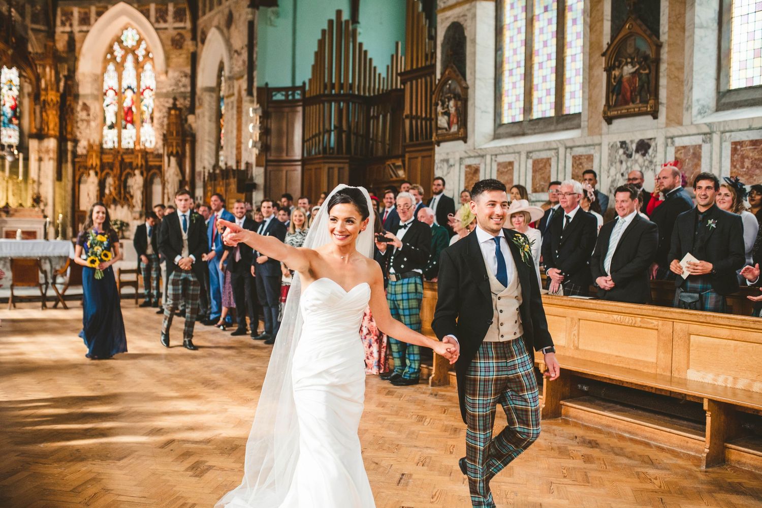 Couple walks down church aisle as guests look on during traditional Scottish wedding.