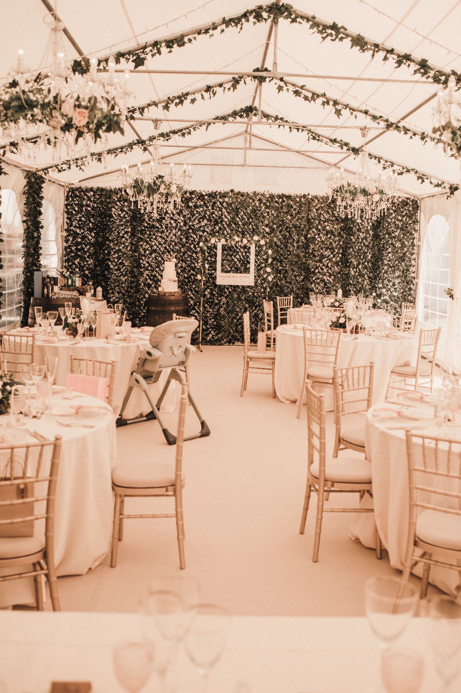 Wedding reception tent decorated with hanging greenery and fairy lights.