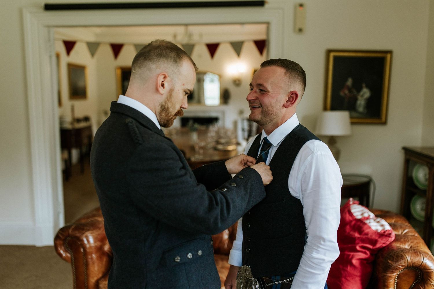 Groomsmen in formal attire share a lighthearted moment indoors.