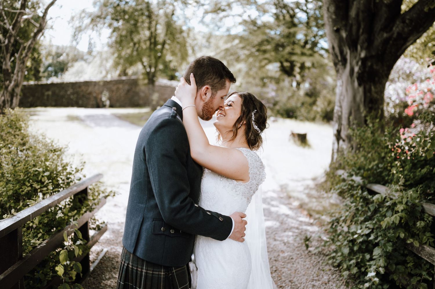 A romantic wedding moment captured on a garden path with flowing white dress and traditional Scottish kilt.