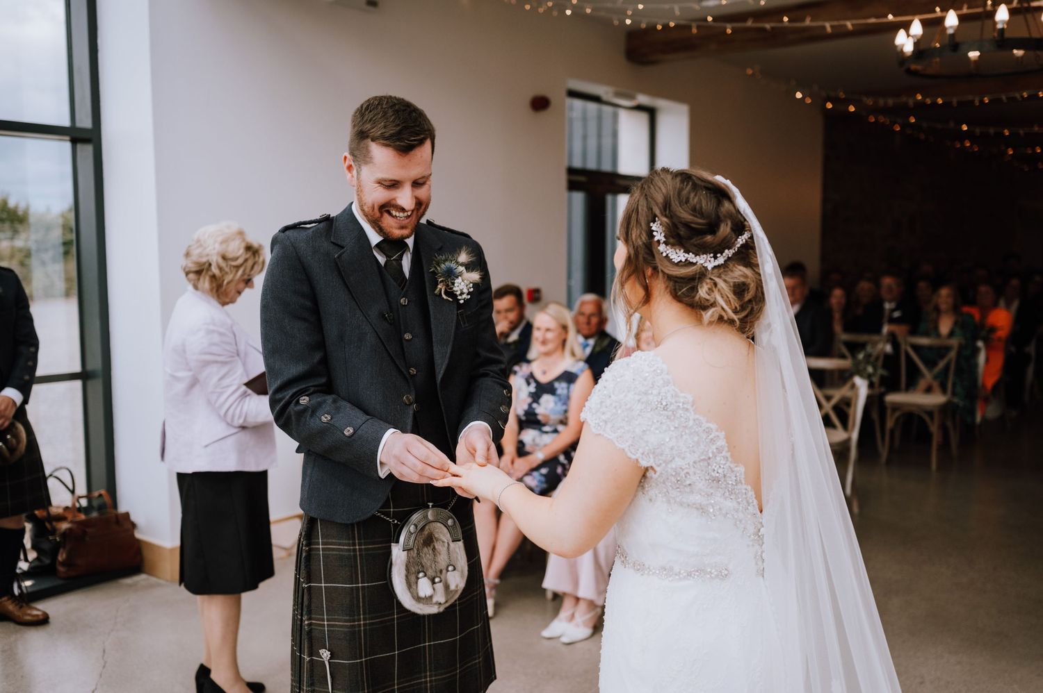 Traditional Scottish wedding ceremony with groom in kilt exchanging rings in rustic venue.