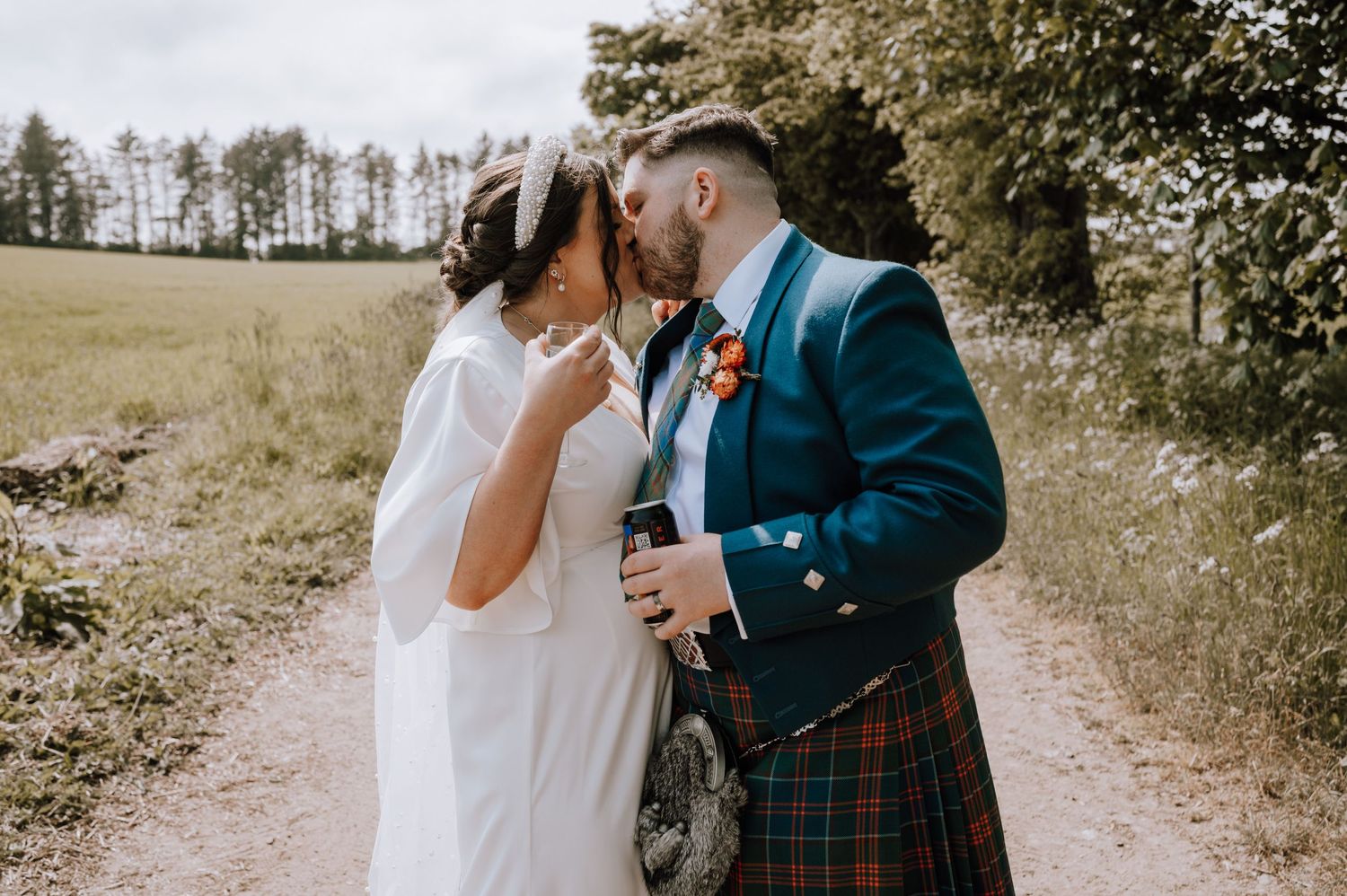 Intimate moment between newlyweds on country path with Scottish highland attire.