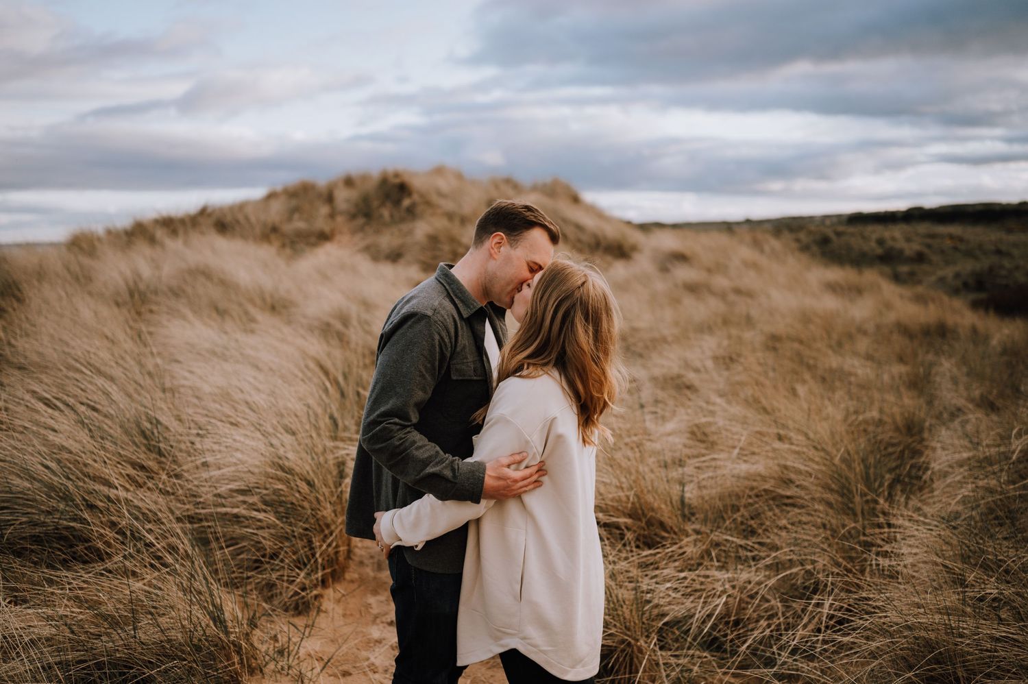 Couple walking through beach grass on sand dunes near the ocean.