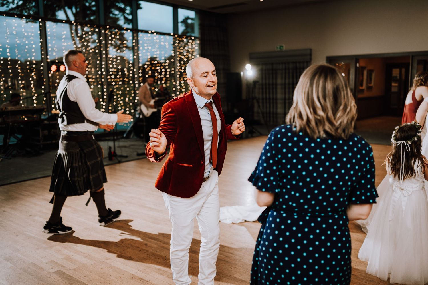 Wedding guests dancing in a venue with fairy light decorations and wooden floors.