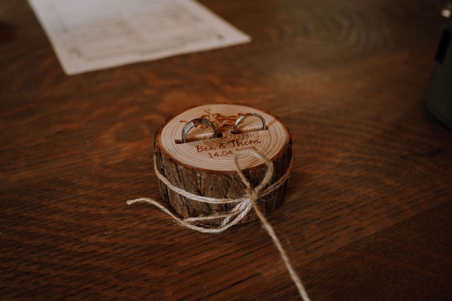 A wooden circular box with twine tied around it sits on a dark wooden surface.