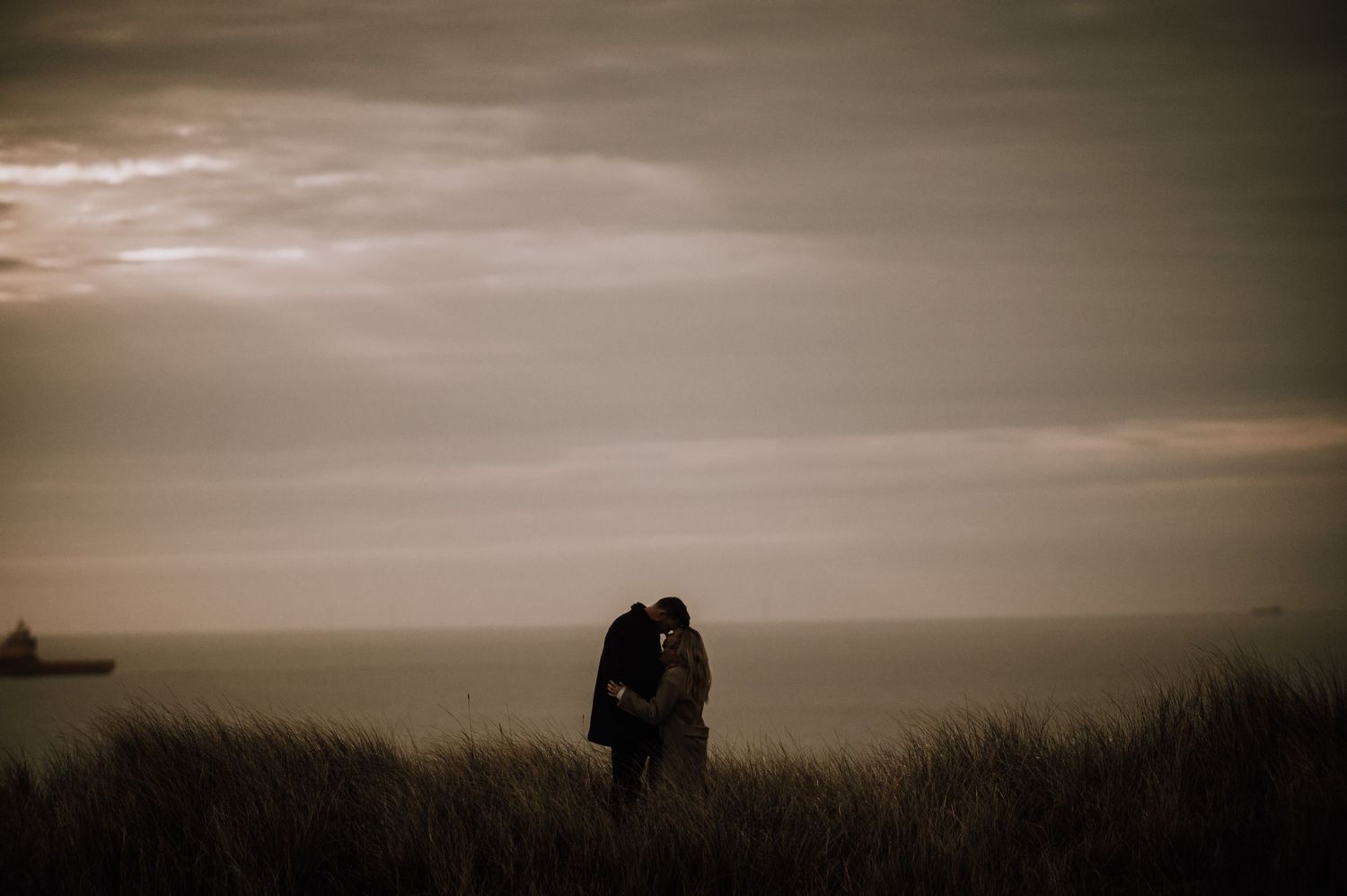A silhouetted couple embraces against a moody coastal sunset sky.