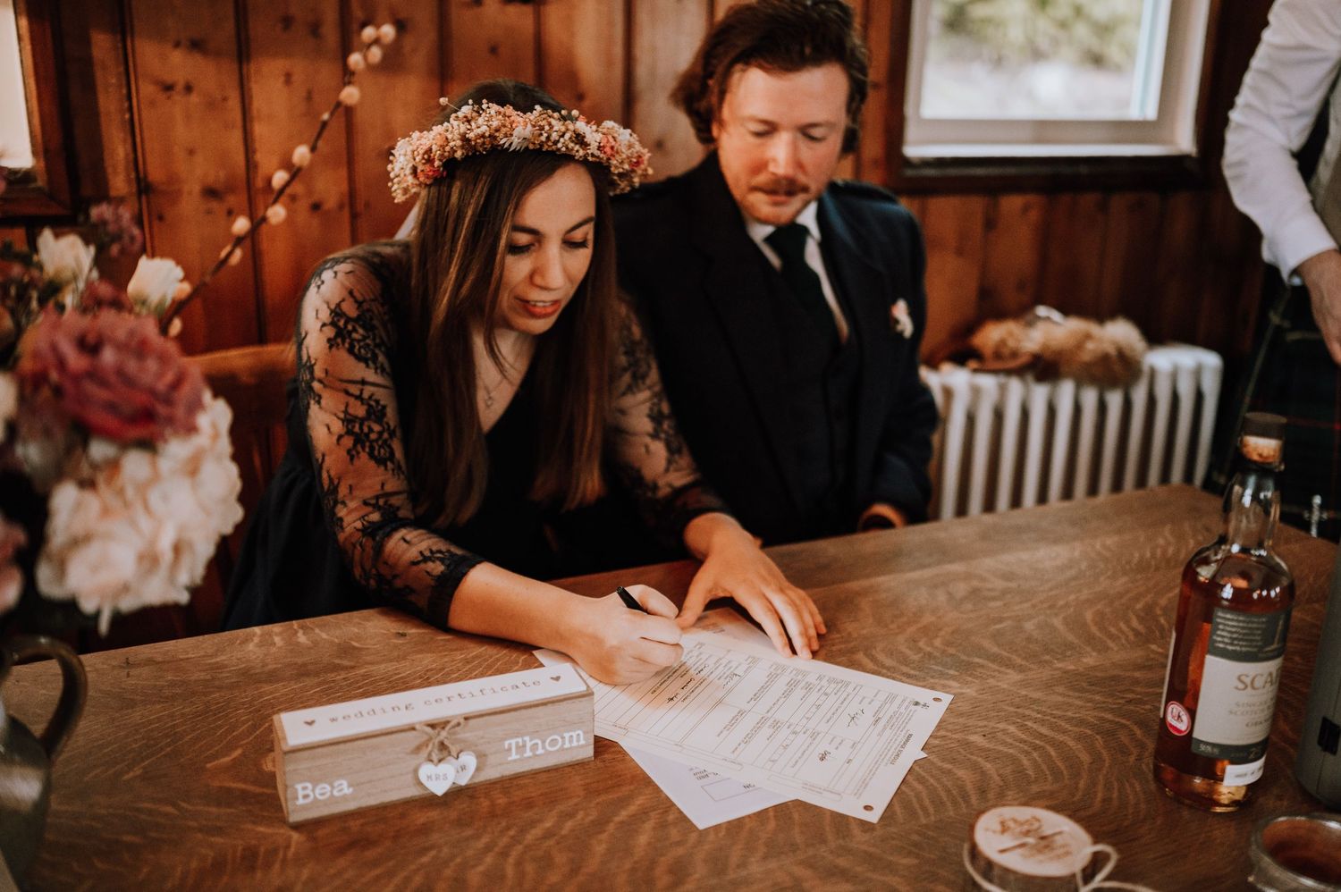 Couple reviewing wedding documents at wooden table in rustic indoor setting.
