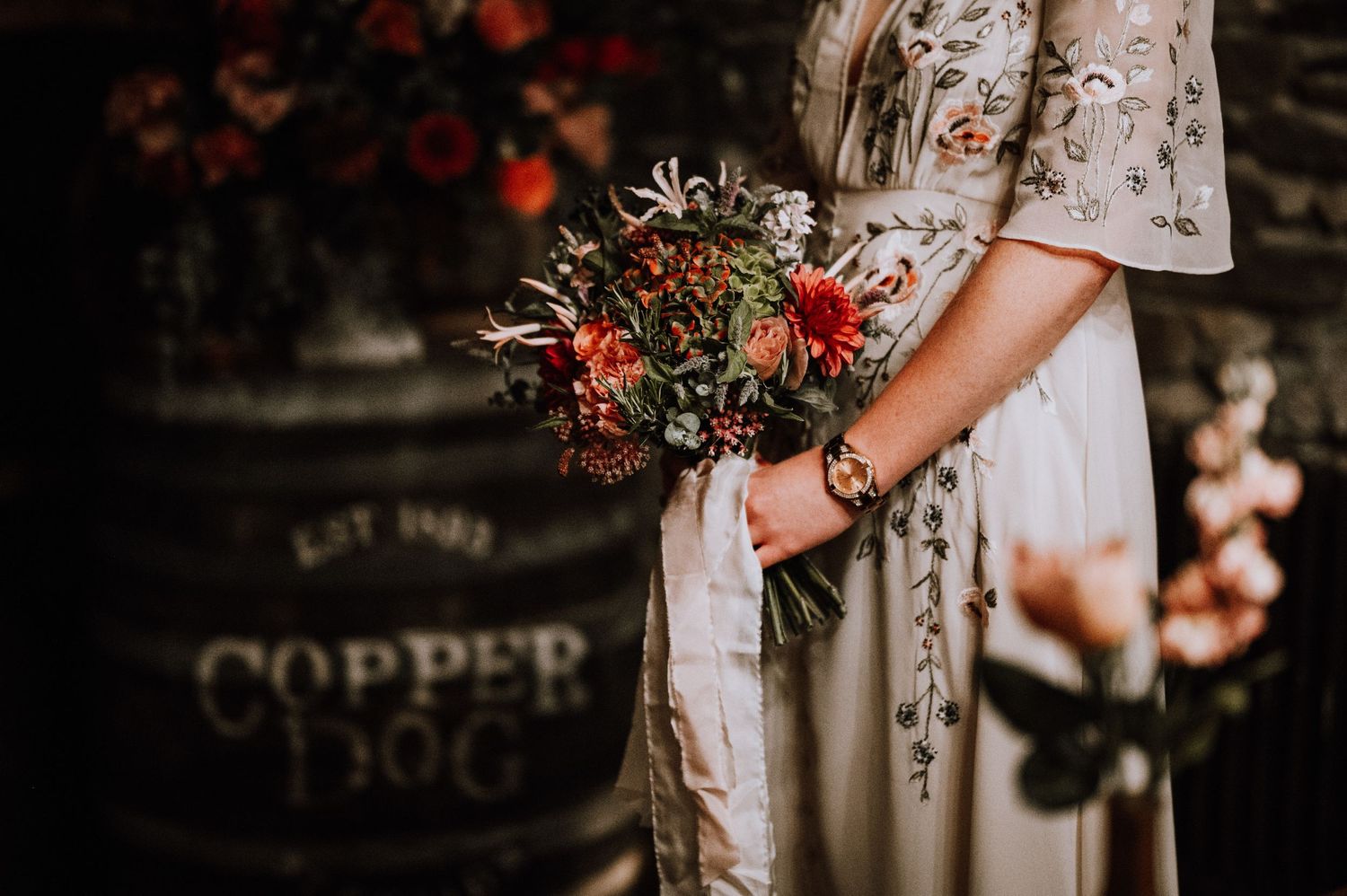 Vintage-style floral bouquet held against a white lace dress near a copper sign.