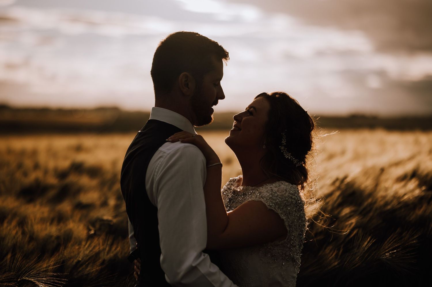 Silhouetted couple shares an intimate moment in a sun-drenched field at sunset.