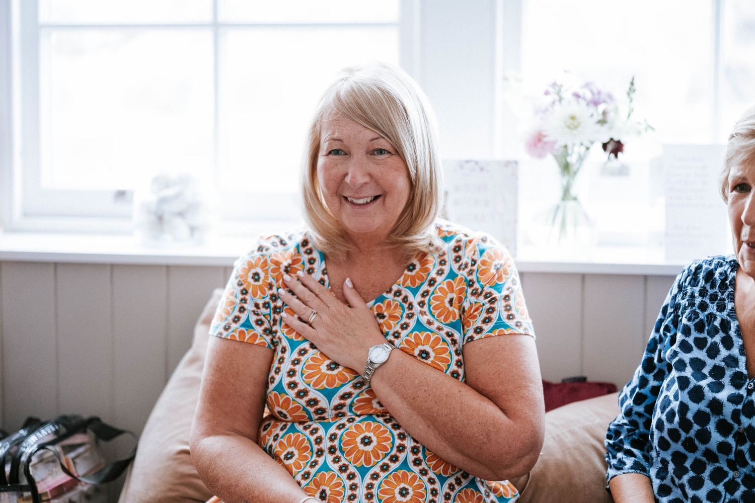 A person wearing a floral print dress sits smiling in a bright interior setting.