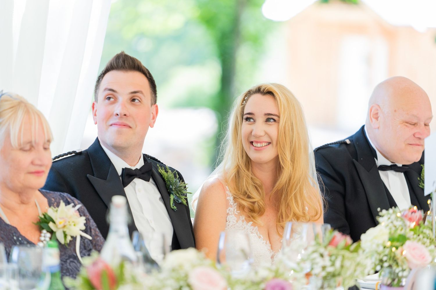 Wedding reception guests enjoying formal dinner in elegant white tent setting.