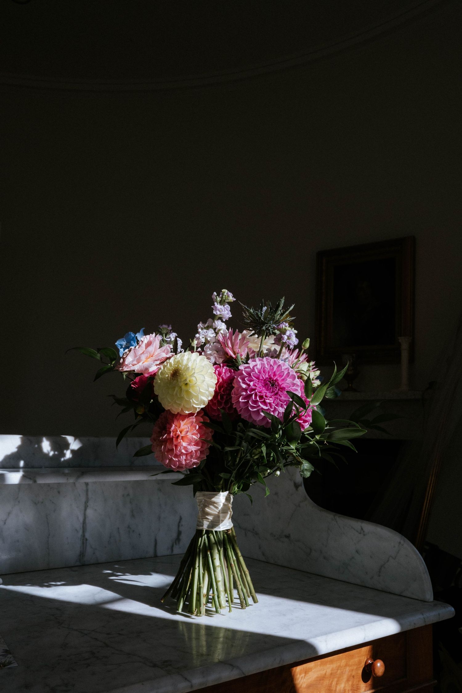 Romantic floral arrangement with pink and white blooms sitting on marble in moody lighting.