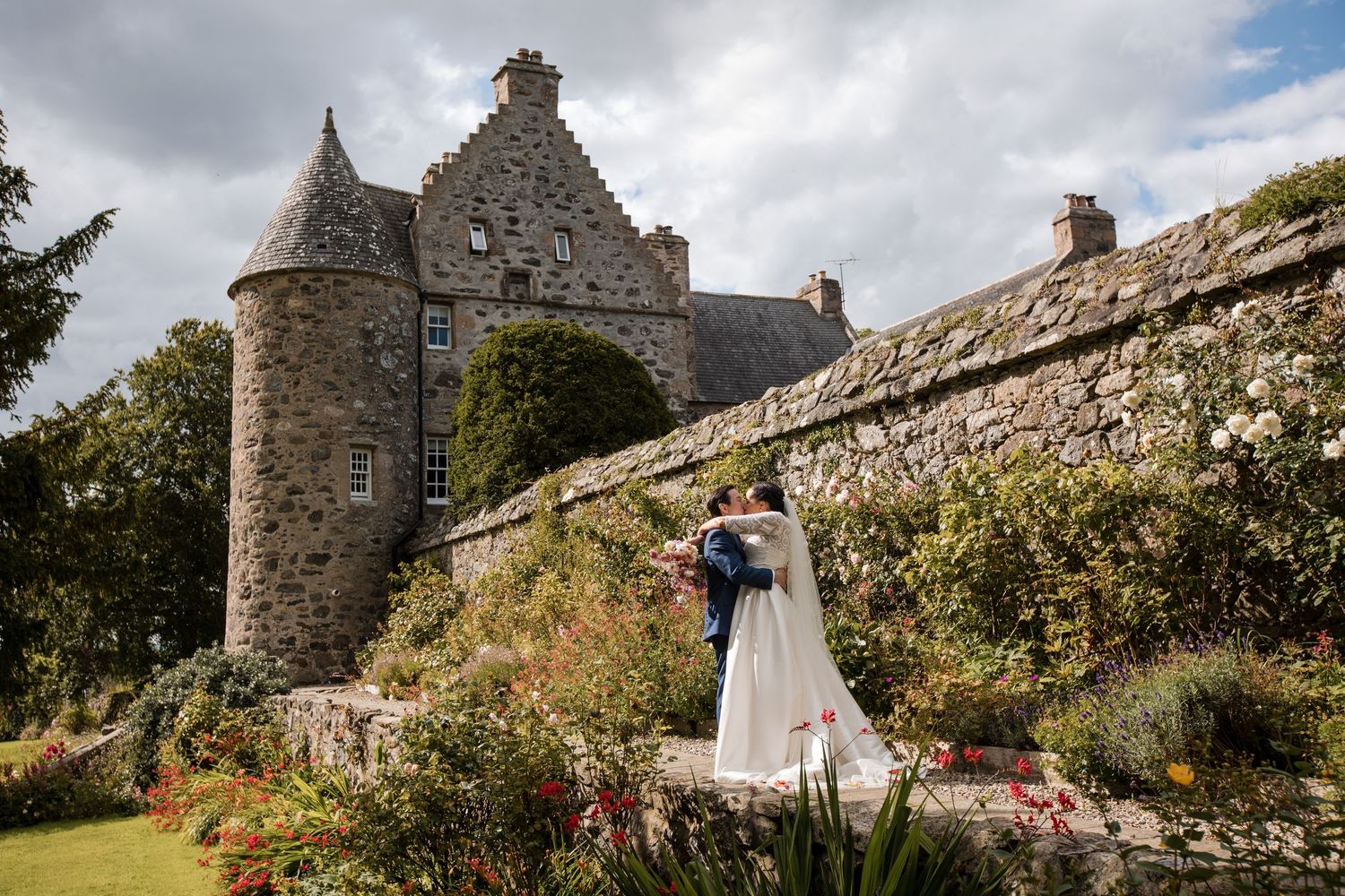 Stone castle wedding venue with dramatic cloudy sky and flowering gardens.