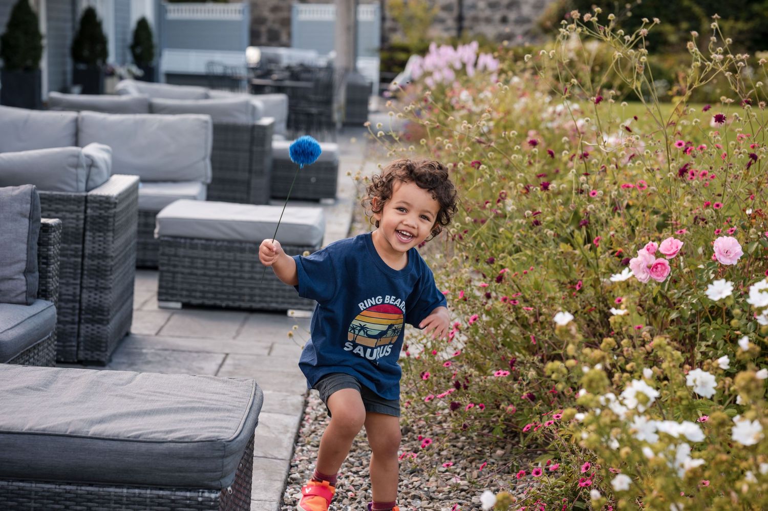 Wildflowers bloom in pink and white colors beside outdoor patio furniture on a sunny day.