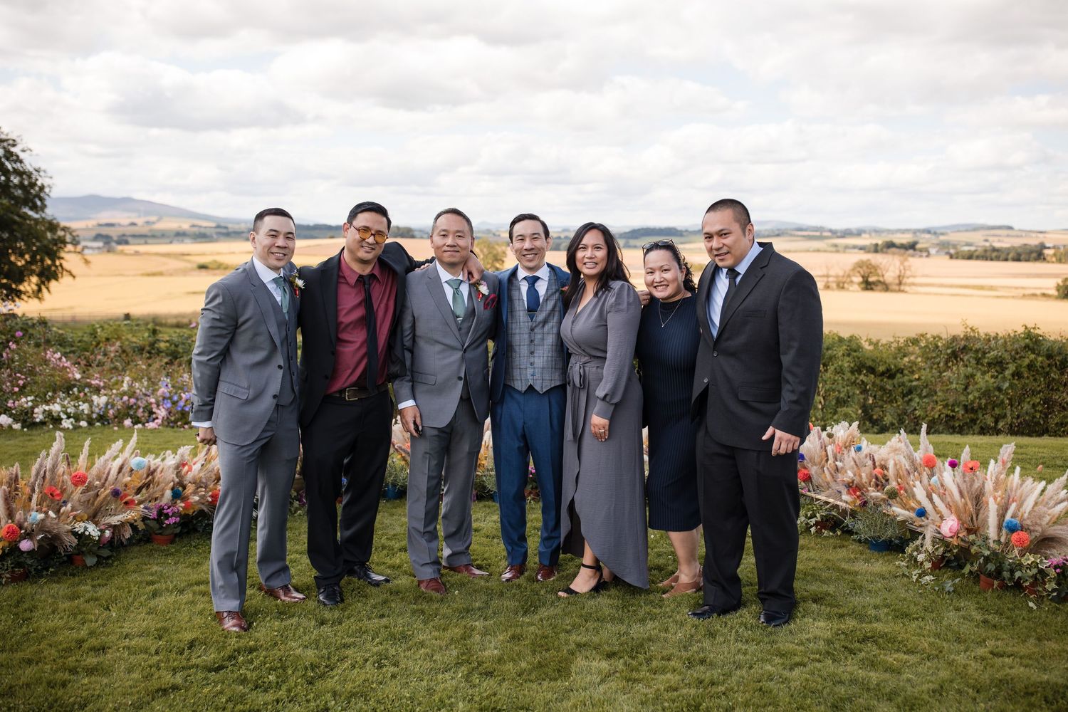 Group photo of wedding party members posing together in a scenic countryside setting.