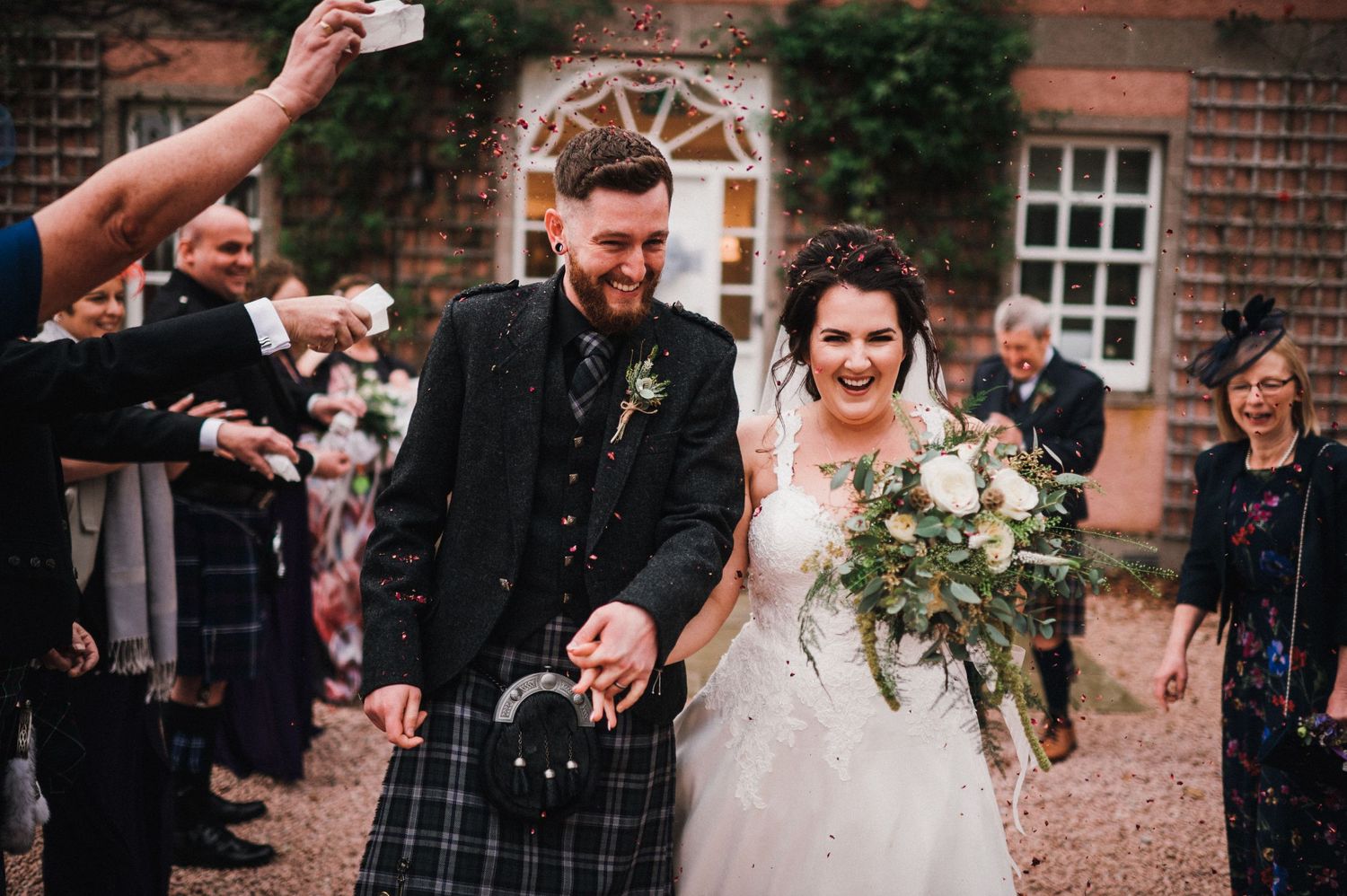 Guests shower newlyweds with confetti outside historic brick building during celebration.