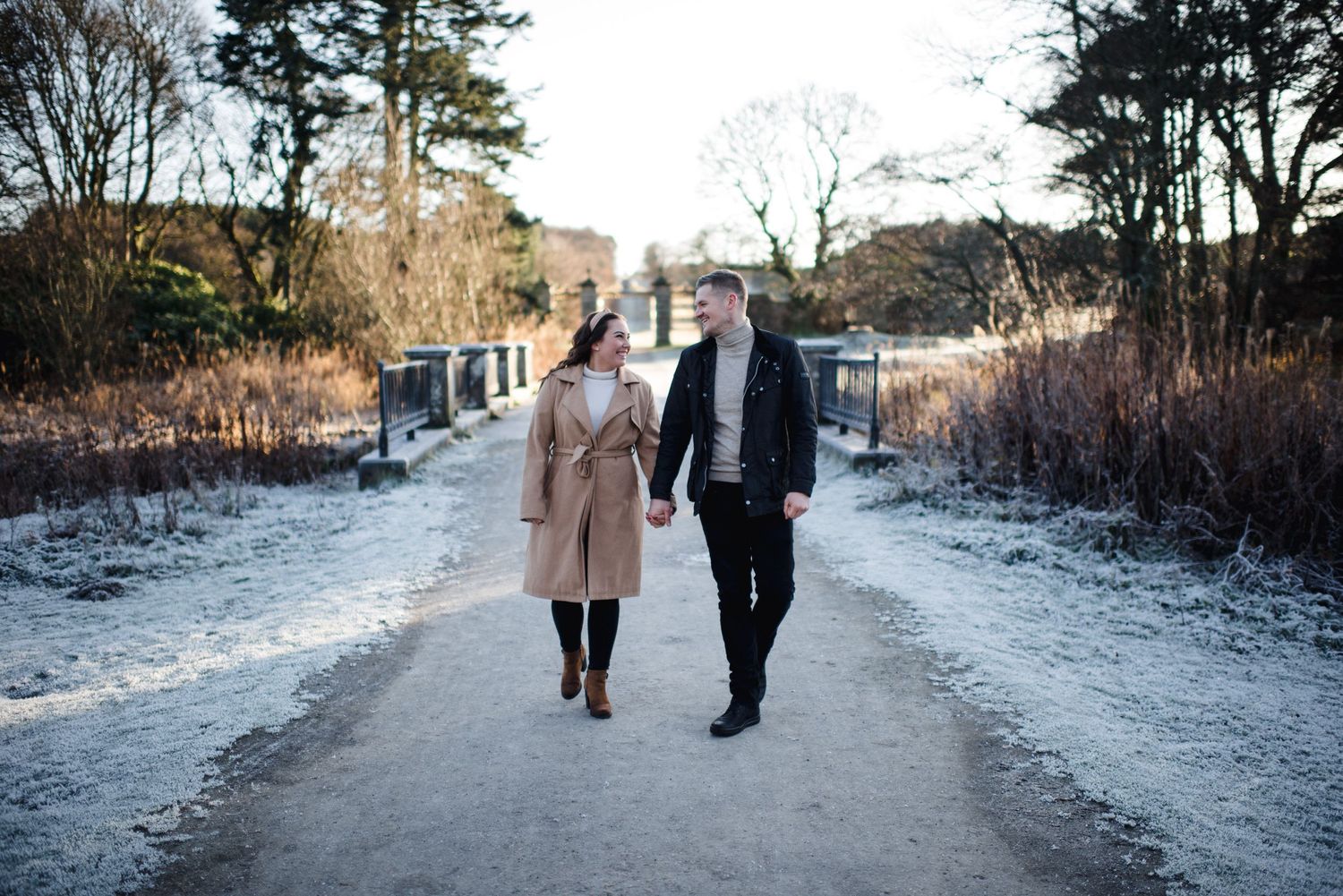 A couple walks hand in hand down a snowy winter path between bare trees.