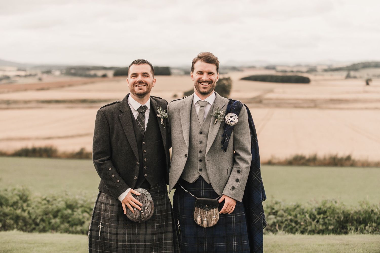 A traditional Scottish wedding on a hilltop with two people wearing kilts and formal attire standing together.