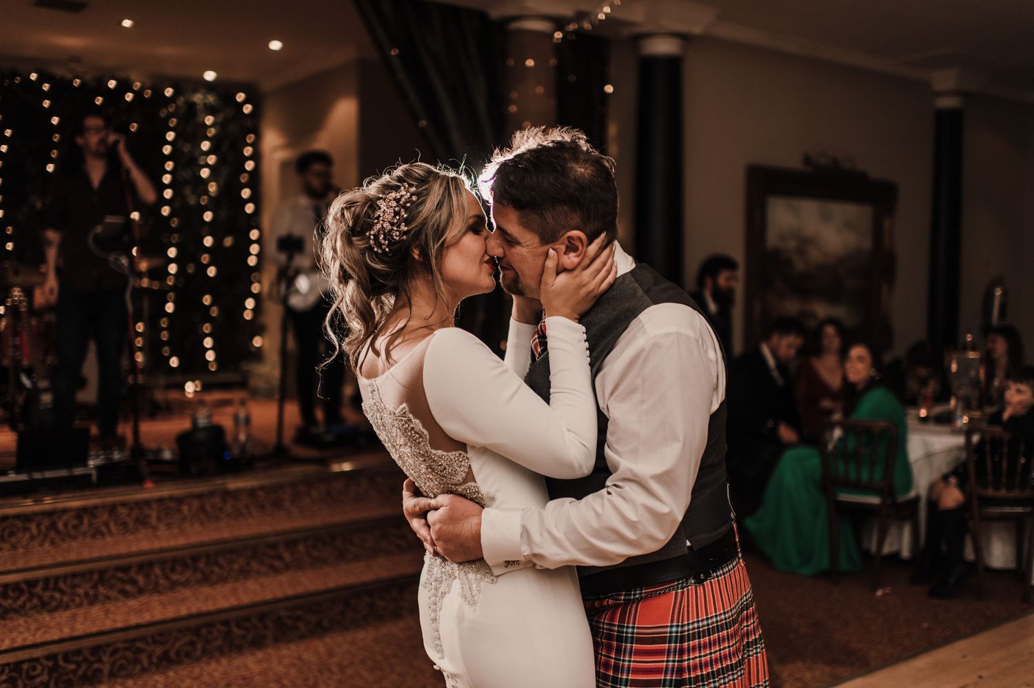 A romantic moment during a wedding dance with traditional Scottish attire and twinkle lights.