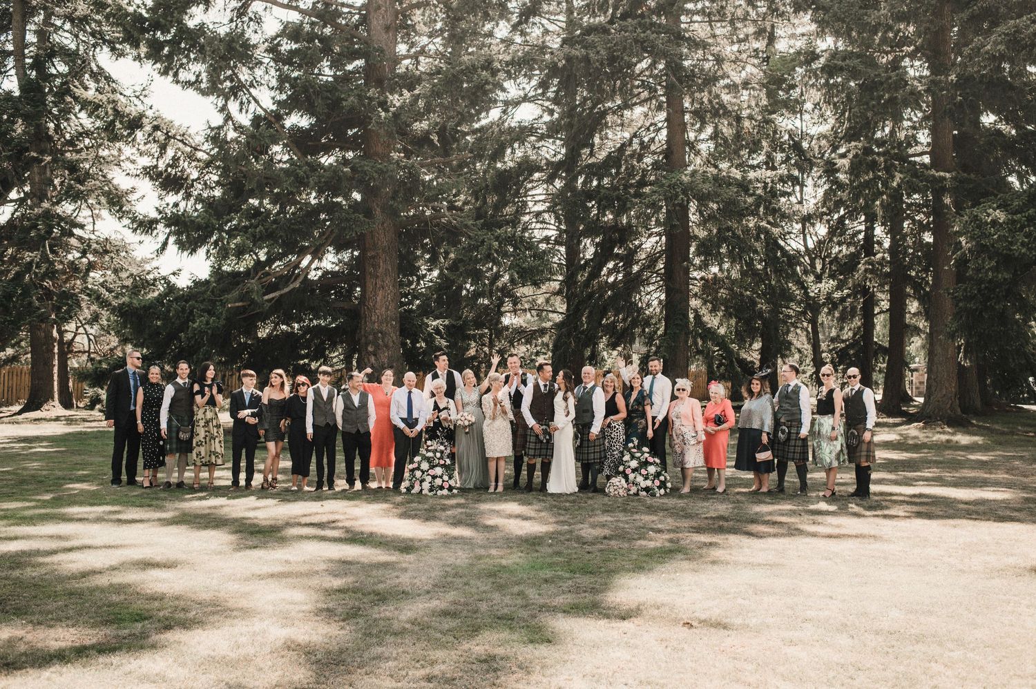 Wedding guests gathered for a group photo in a wooded outdoor venue.