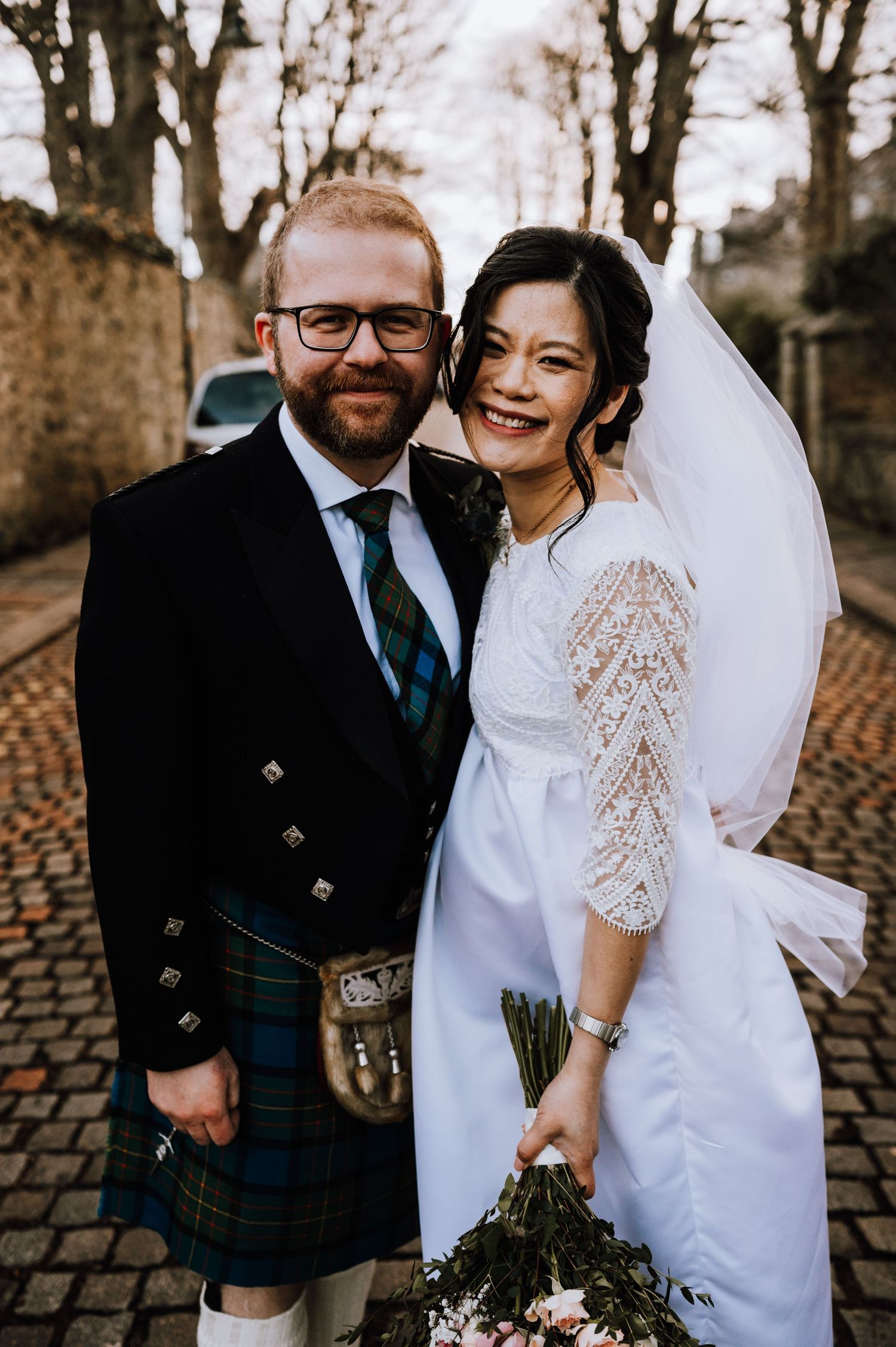 A joyful wedding portrait featuring Scottish and Asian fusion wedding attire against an autumn backdrop.