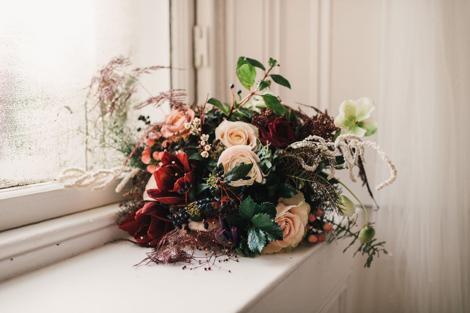 Vintage-inspired wedding bouquet with roses and greenery sitting on a white windowsill.