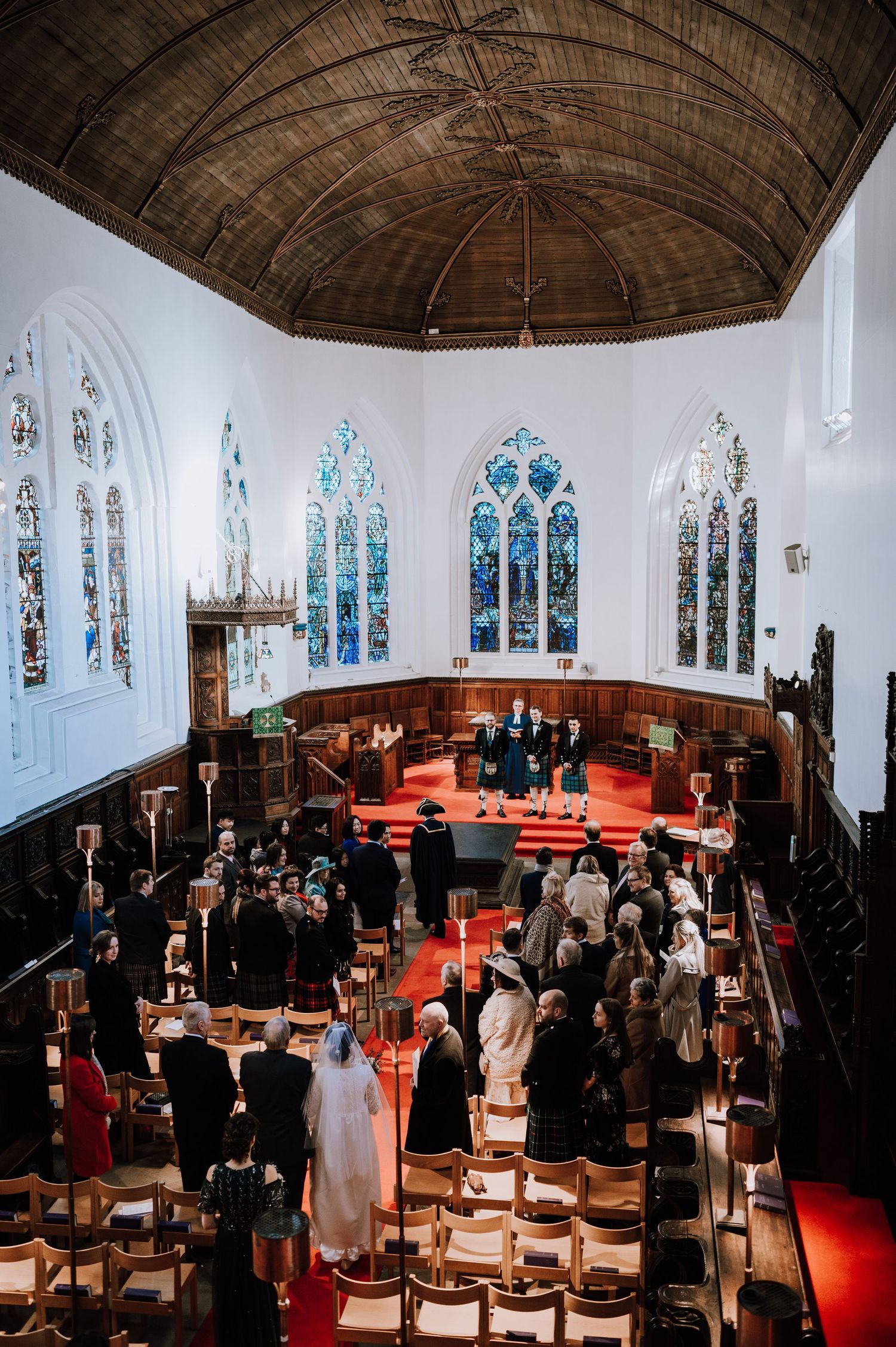 Wedding ceremony in historic church with vaulted ceiling and stained glass windows.