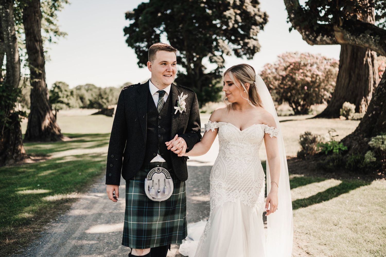 Scottish wedding couple walking together on garden path with groom in traditional kilt.