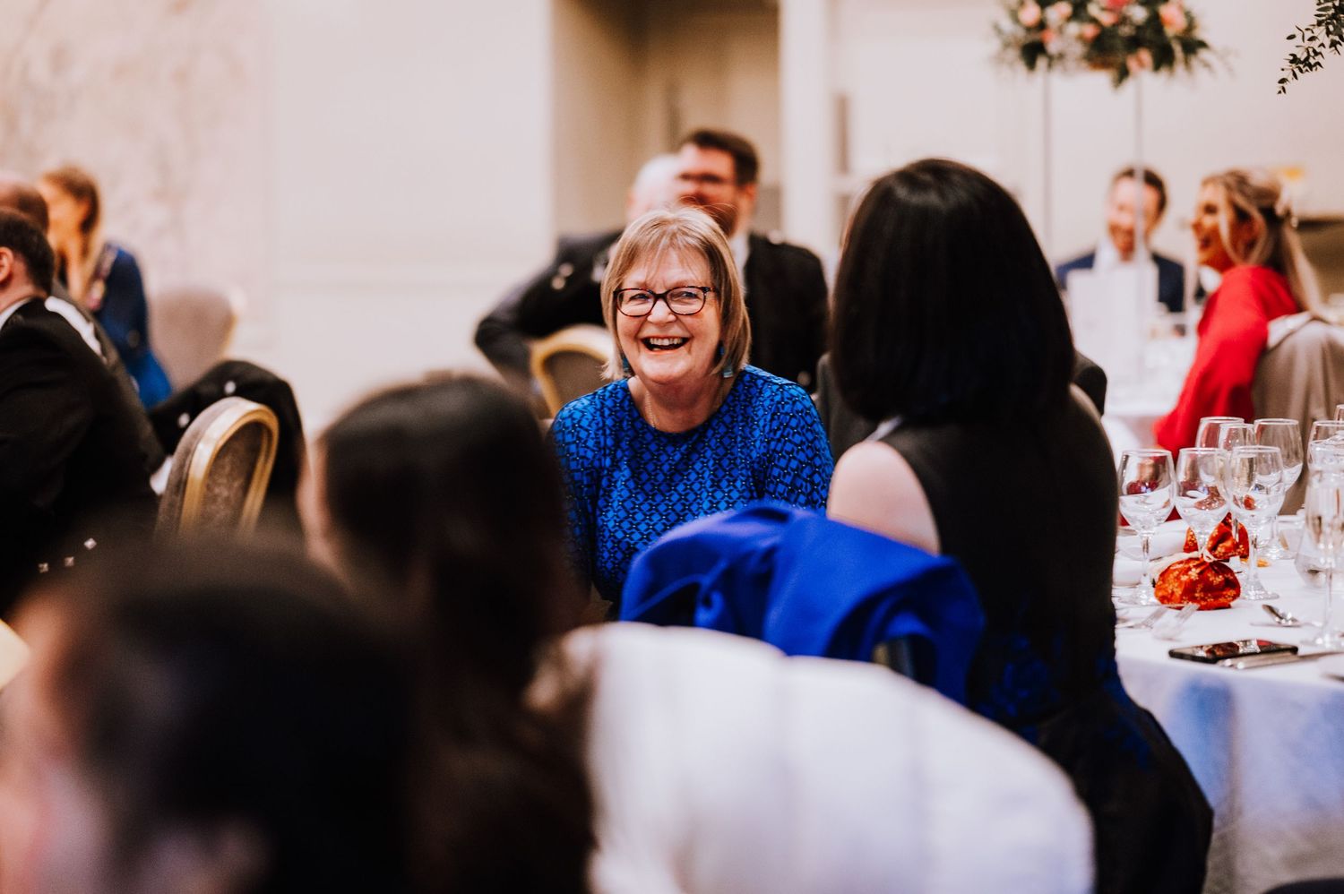 Guest in bright blue dress enjoying conversation at wedding reception.