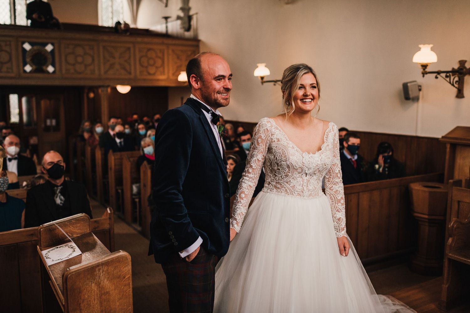 A wedding ceremony in a church with wooden panels and wall sconces.