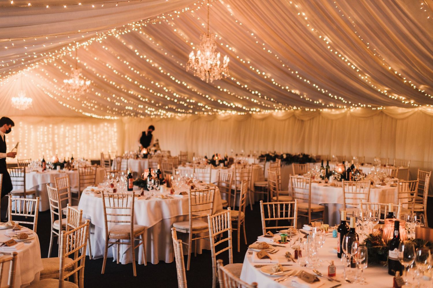 Elegant wedding reception venue with draped ceiling, twinkling lights and white table settings.