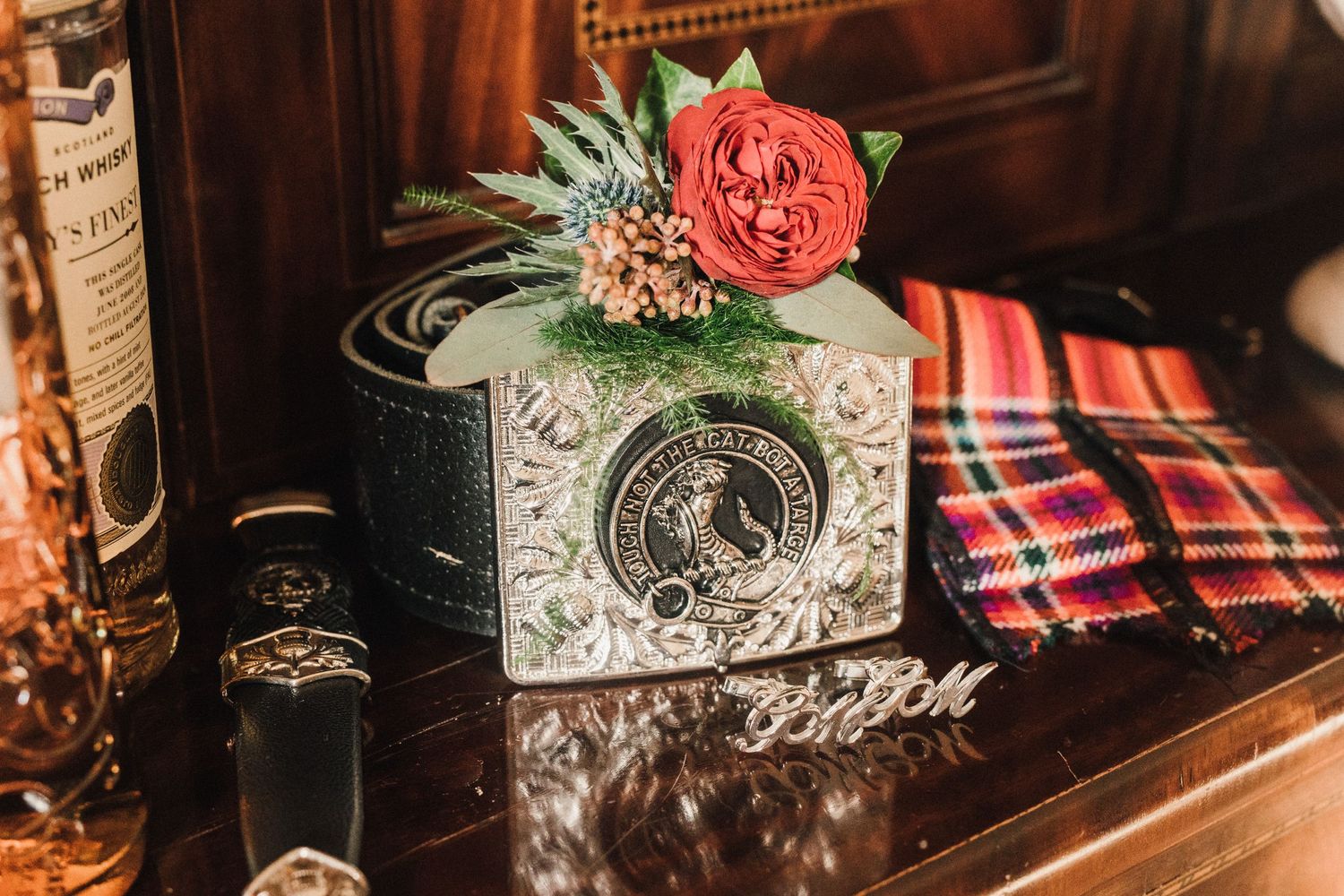 Decorative box with floral arrangement featuring a red rose and greenery on plaid fabric.