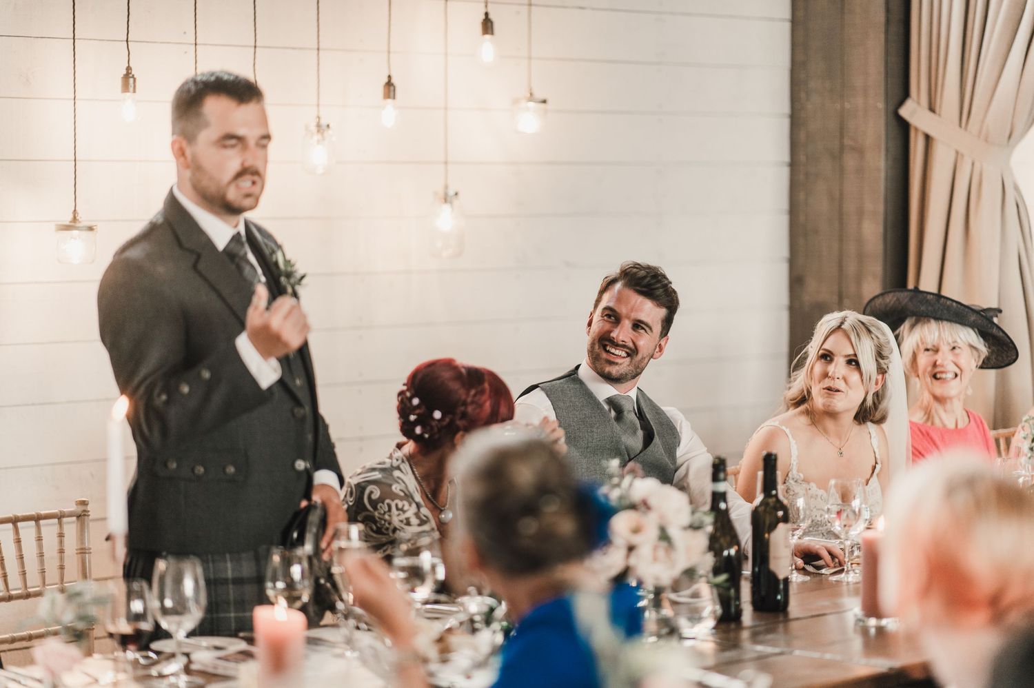 A celebratory moment during wedding speeches with guests laughing at an elegant reception venue.